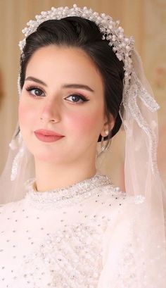 a woman wearing a wedding dress and veil with pearls on her head, posing for the camera