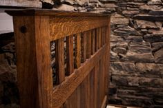 a close up of a wooden bed headboard with stone walls in the back ground