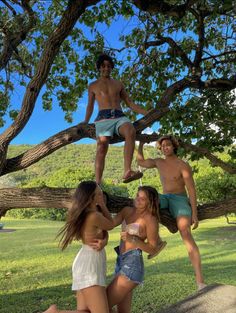 four young people hanging out in the shade on a tree branch with one man standing up and two women sitting down