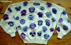 a white sweater with purple and blue flowers on the front is sitting on a wooden floor