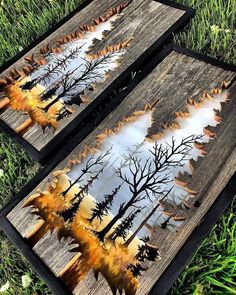 two pieces of wood that have been painted with trees and leaves on them, sitting in the grass