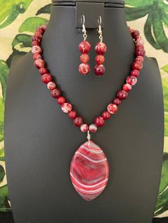 You will receive a gorgeous, red, banded agate marquis-shaped pendant necklace and a pair of matching earrings.   This spectacular banded agate pendant has markings that include shades of red, dark red, white, and a bit of gray.  It is strung entirely with color-matched red and white fire agate beads.   The 17-inch necklace has a toggle clasp, making it very easy to put on by yourself. The stunning, wonderfully-banded, flat-back pendant measures 2 3/4 inches in length from bail to bottom and is Red Gemstone Necklace, Red Gemstone Jewelry, Red Agate Necklace, Red Necklace, Necklace Red, Fire Agate, Red Gemstones, Red Dark, Agate Jewelry