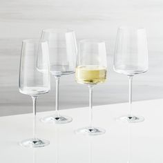 four wine glasses are lined up on a white counter top, with one empty glass in the middle