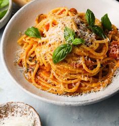 a white bowl filled with pasta and topped with parmesan cheese, basil leaves