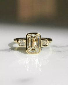 an emerald and baguette diamond ring on a white surface with gold trimming