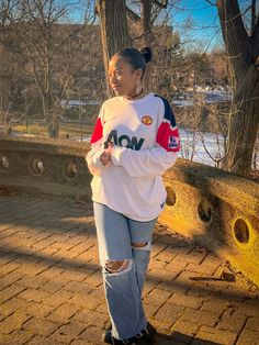 a woman standing in front of some trees wearing a white and red sweatshirt with the word aon on it