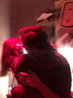 a man and woman embracing in front of a clock on the wall with red light coming from behind them