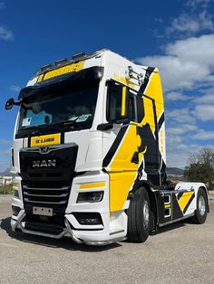 a yellow and white semi truck parked in a parking lot next to a blue sky