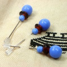 some blue and brown beads are laying on a piece of fabric next to two pins