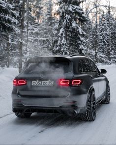 the rear end of a car driving down a snow covered road with trees in the background