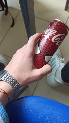 a person holding a can of soda in their left hand while sitting on a blue chair