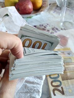 a person holding money in their hand on top of a table with fruit and napkins