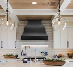 a kitchen with white cabinets and two hanging lights over the stove top, surrounded by marble counter tops