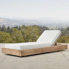 a wooden bed with white sheets on top of a stone floor in front of trees