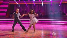 two people dancing on the dance floor in front of purple lights with their arms around each other