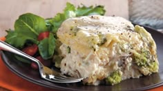 a black plate topped with broccoli and cheese covered casserole next to a salad