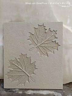 two carved leaves are shown on the side of a white tile wall, one is made out of cement and the other has an intricate carving technique