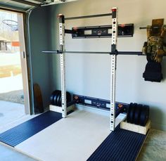 a garage gym with two squat racks and three dumbs on the floor, in front of a sliding glass door