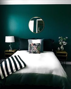 a bed with black and white pillows in front of a mirror on the wall above it