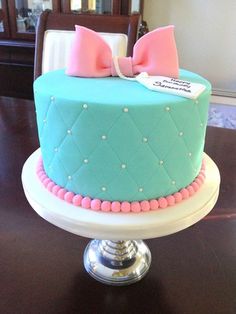 a blue cake with pink and white decorations on it sitting on top of a table