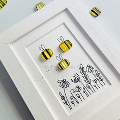 three yellow and black striped bees in a white frame on a table next to flowers