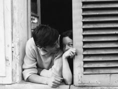 a man and woman leaning on the window sill looking into each other's eyes