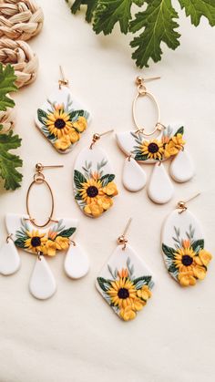 six sunflowers and tear drop earrings on a white surface with green leaves in the background