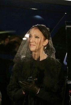 a woman in a black dress and veil on her head is looking off to the side