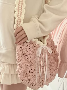 a woman holding a pink crocheted purse with a white ribbon around the handle