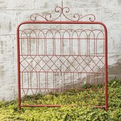 a red iron bed frame sitting on top of a lush green grass covered ground next to a white brick wall