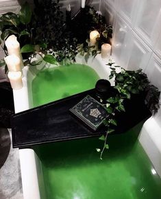 a green bathtub with candles and plants in the tub, next to it is a book