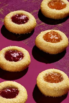 several cookies with jam in the middle on a pink surface