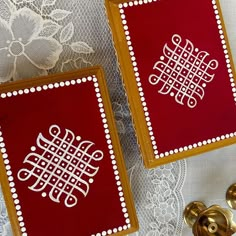 two red and gold coasters sitting on top of a lace covered tablecloth next to golden knobs