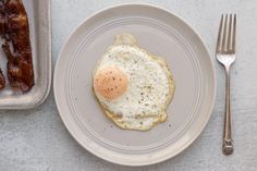 an egg is sitting on top of a plate next to some bacon and a fork