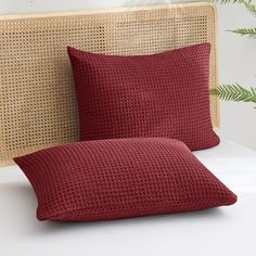 two red pillows sitting on top of a bed next to a headboard with plants in the background