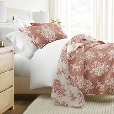 a bed with pink and white comforters in a bedroom next to a window,