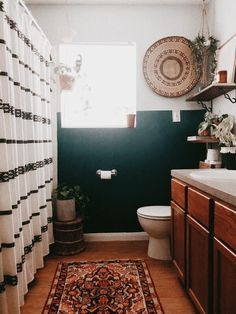 a white toilet sitting next to a sink in a bathroom under a window with a rug on the floor