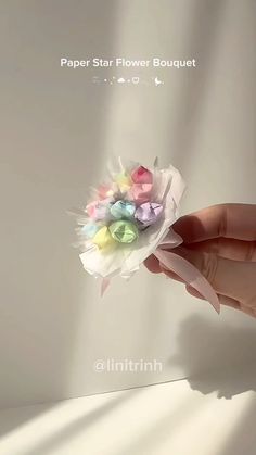 a hand holding a paper flower bouquet with pastel flowers in it's center