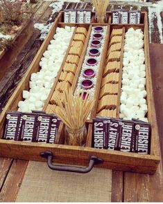 an open wooden box filled with marshmallows and other items on top of a table