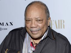 an older man wearing a black jacket and striped tie smiles at the camera while standing in front of a white backdrop