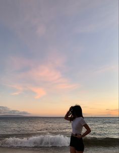 a woman standing on top of a sandy beach next to the ocean at sunset or dawn