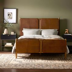 a bed with white pillows and brown leather headboard in a green walled bedroom area