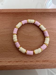 a pink and white beaded bracelet sitting on top of a wooden table