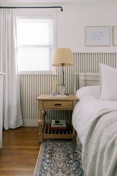 a bedroom with a bed, nightstand and window in the corner next to a lamp