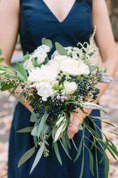 a woman in a blue dress holding a bouquet of white flowers and greenery on her wedding day