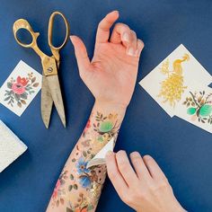 a woman's arm with tattoos and scissors on it, next to some cards