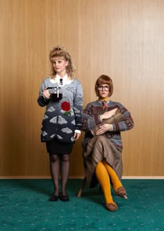 two women are posing for a photo in front of a wood paneled wall and green carpet