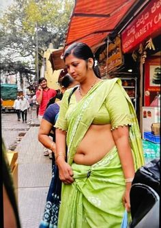 a woman in a green sari is standing on the street with her belly exposed