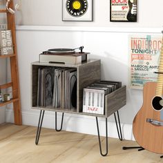 a record player is sitting next to a shelf with records on it and a guitar leaning against the wall