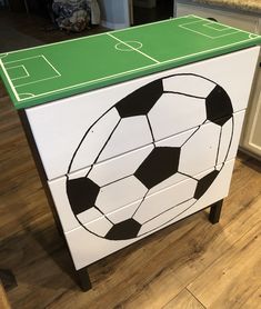 a soccer ball painted on the side of a white dresser in a kitchen with wood floors